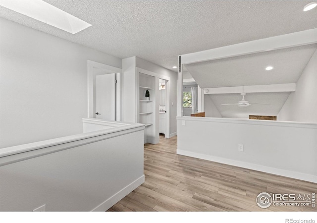 corridor with wood finished floors, baseboards, a skylight, recessed lighting, and a textured ceiling