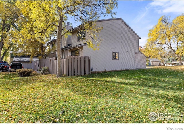 view of side of property with a yard, a chimney, and fence