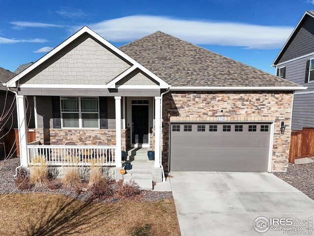 view of front of house with a porch, roof with shingles, driveway, stone siding, and an attached garage