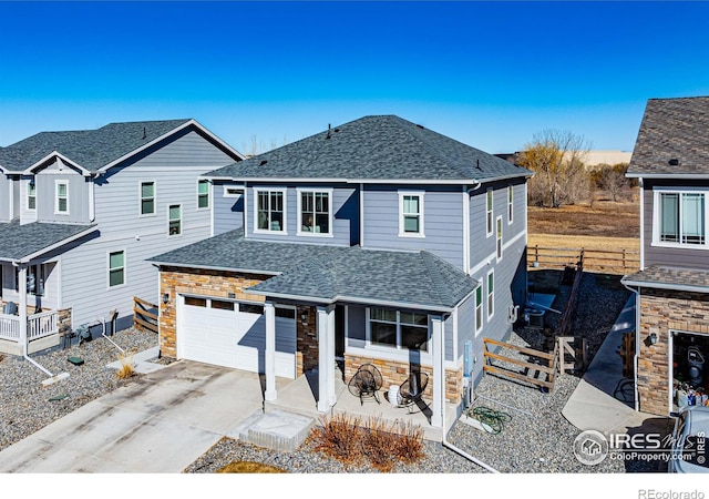 traditional-style home with driveway, stone siding, fence, an attached garage, and a shingled roof