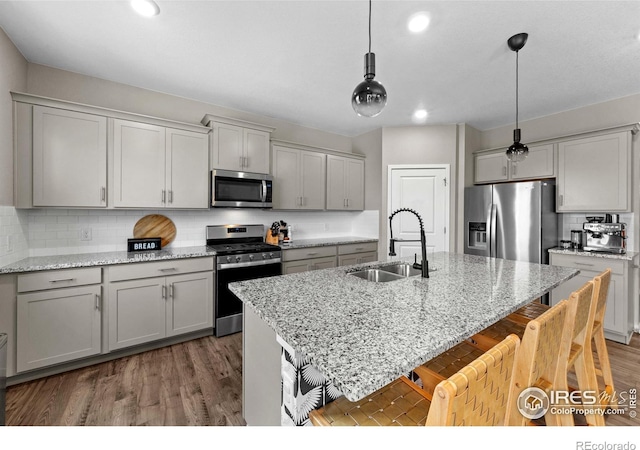 kitchen featuring appliances with stainless steel finishes, a sink, decorative light fixtures, decorative backsplash, and a kitchen bar