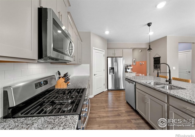 kitchen with decorative backsplash, dark wood-style flooring, light stone countertops, a sink, and stainless steel appliances
