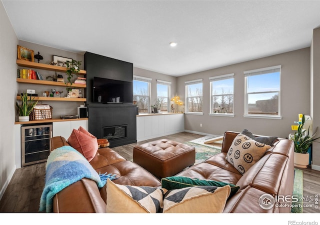 living room with a glass covered fireplace, baseboards, beverage cooler, and wood finished floors