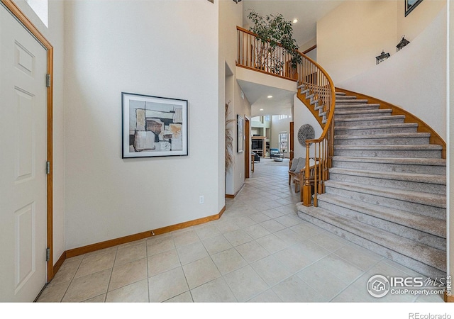 entryway with light tile patterned floors, stairway, baseboards, and a high ceiling