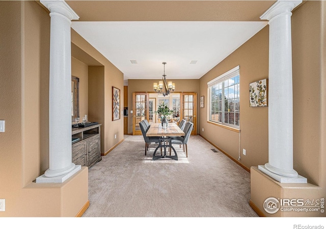 dining room with a notable chandelier, light colored carpet, baseboards, and ornate columns