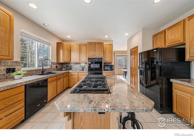 kitchen with black appliances, a sink, backsplash, a kitchen island, and a breakfast bar area