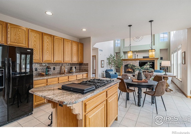 kitchen with a kitchen island, a warm lit fireplace, black appliances, open floor plan, and tasteful backsplash