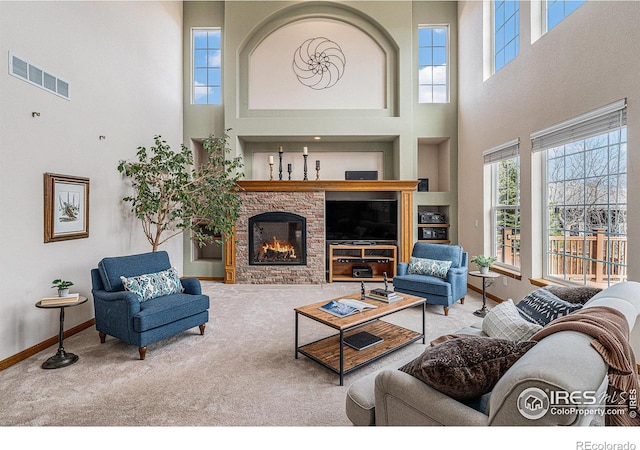 carpeted living area featuring visible vents, built in features, a stone fireplace, baseboards, and a towering ceiling