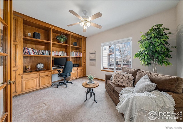 office space with light carpet, built in desk, baseboards, and ceiling fan