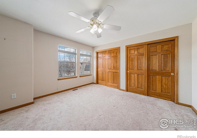 unfurnished bedroom featuring visible vents, baseboards, multiple closets, ceiling fan, and carpet flooring