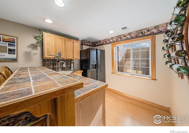 kitchen featuring visible vents, light wood-type flooring, a sink, black fridge with ice dispenser, and tile countertops