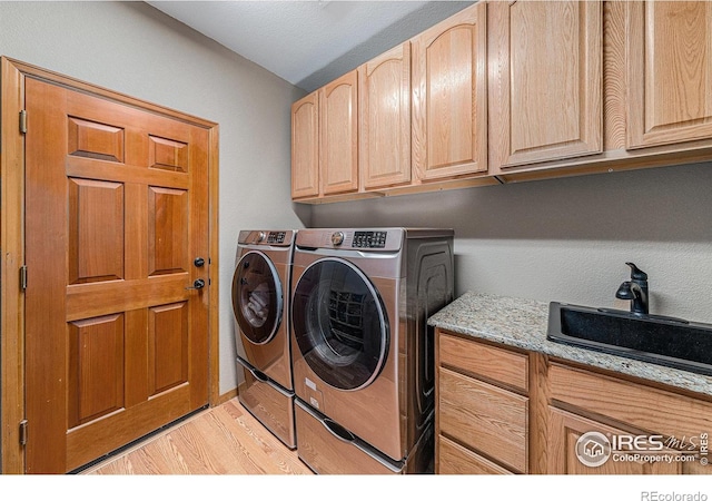 laundry room featuring washer and clothes dryer, light wood-style flooring, cabinet space, and a sink