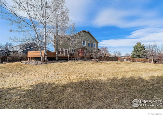 rear view of property with a wooden deck, a lawn, and fence