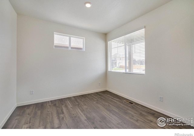 unfurnished room featuring dark wood-style floors, visible vents, and baseboards