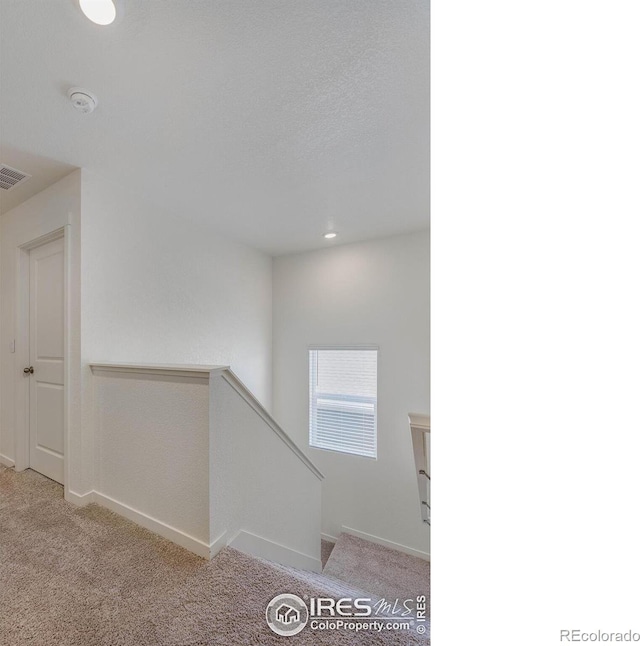 corridor featuring an upstairs landing, visible vents, baseboards, and carpet