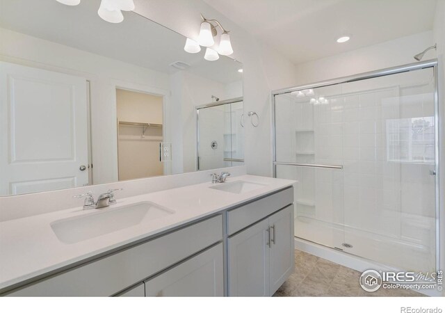 bathroom with double vanity, a spacious closet, a stall shower, and a sink