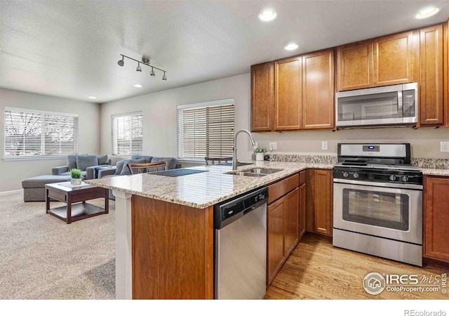 kitchen with a peninsula, a sink, open floor plan, appliances with stainless steel finishes, and brown cabinets