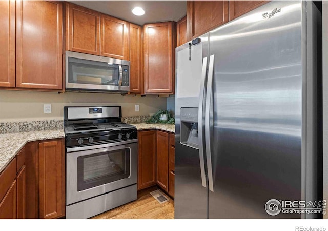 kitchen featuring light stone countertops, visible vents, stainless steel appliances, light wood-style floors, and brown cabinets