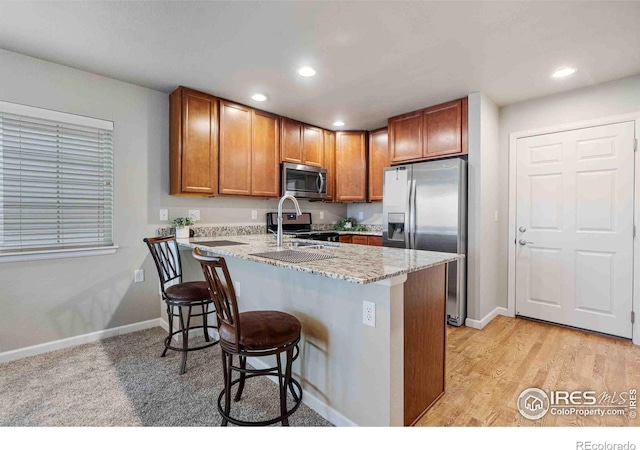 kitchen featuring brown cabinetry, a peninsula, a sink, stainless steel appliances, and a kitchen breakfast bar