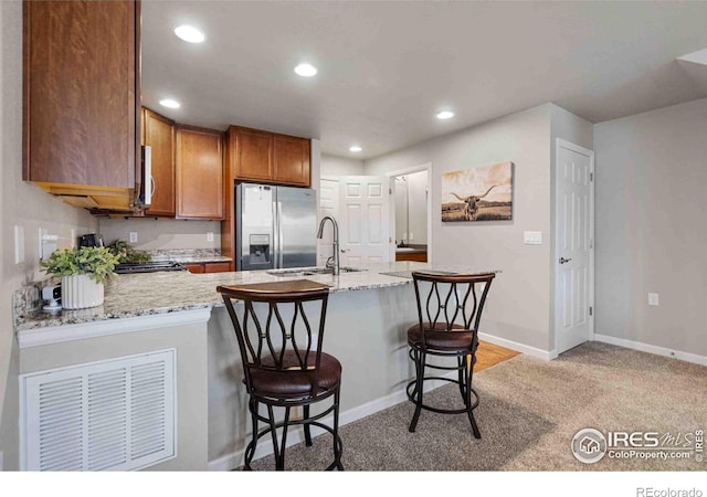 kitchen featuring stainless steel fridge with ice dispenser, recessed lighting, brown cabinets, a peninsula, and a sink