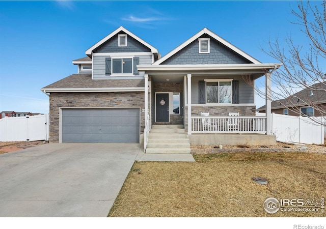 craftsman inspired home featuring fence, an attached garage, covered porch, concrete driveway, and stone siding