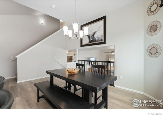 dining space featuring baseboards, wood finished floors, a towering ceiling, and ceiling fan with notable chandelier