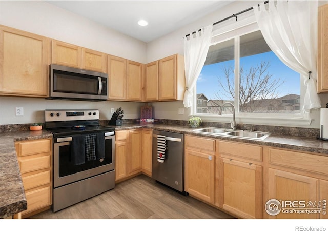 kitchen with a sink, dark countertops, light brown cabinets, and stainless steel appliances