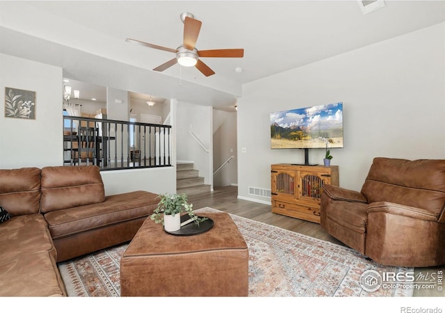 living room featuring stairs, wood finished floors, visible vents, and ceiling fan