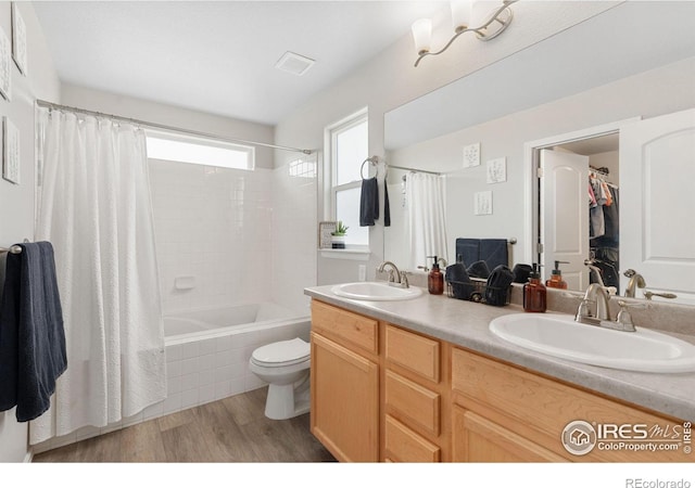 bathroom with double vanity, toilet, wood finished floors, and a sink