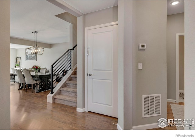 foyer with visible vents, baseboards, stairs, an inviting chandelier, and wood finished floors