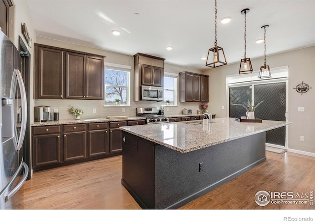 kitchen with a sink, tasteful backsplash, stainless steel appliances, light wood finished floors, and dark brown cabinets