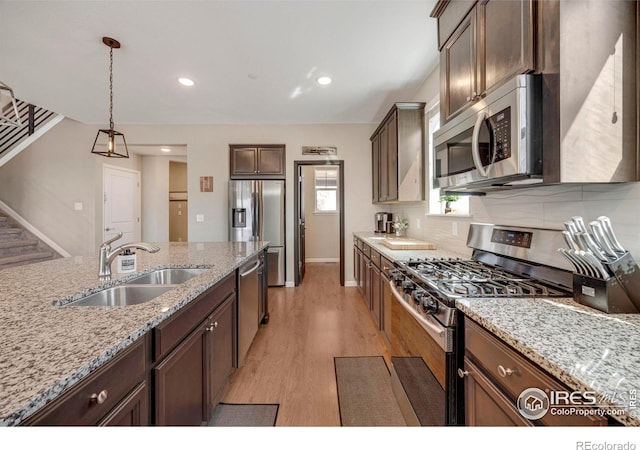 kitchen featuring tasteful backsplash, pendant lighting, light wood-style flooring, stainless steel appliances, and a sink