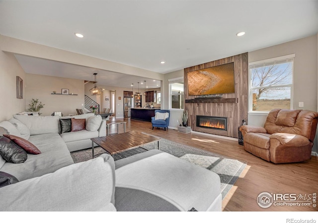 living room with stairs, recessed lighting, wood finished floors, and a large fireplace