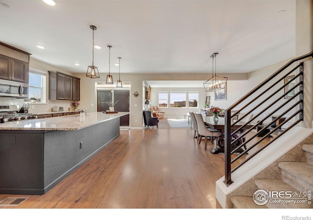 kitchen with light wood-style flooring, light stone counters, decorative light fixtures, stainless steel appliances, and dark brown cabinetry