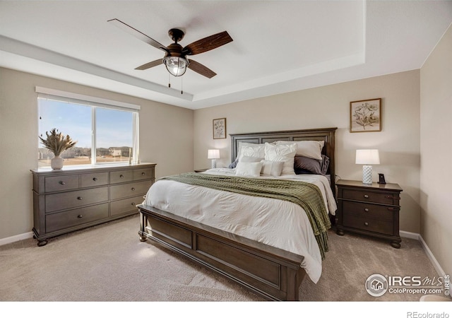 bedroom with light carpet, a ceiling fan, a raised ceiling, and baseboards