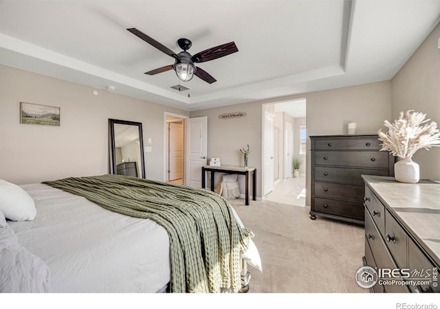 bedroom with visible vents, ceiling fan, a tray ceiling, light carpet, and ensuite bathroom