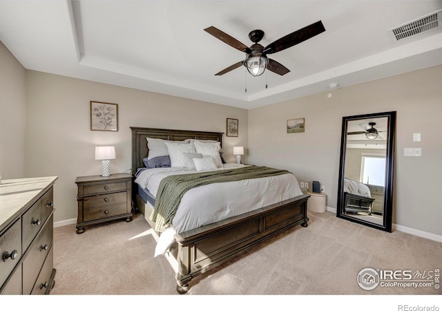 bedroom with light carpet, visible vents, and a raised ceiling