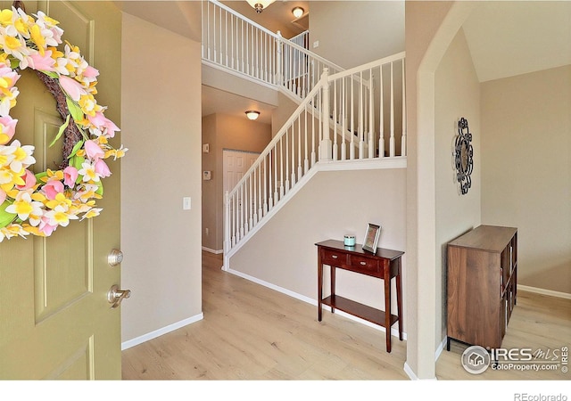 foyer featuring baseboards, stairs, a high ceiling, wood finished floors, and arched walkways