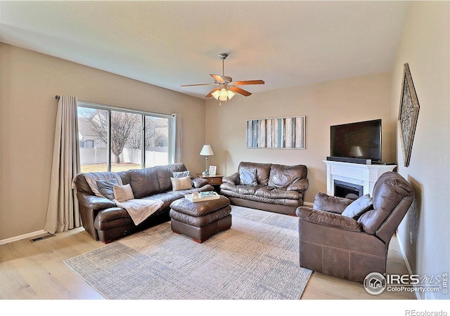 living area featuring a ceiling fan, visible vents, light wood finished floors, baseboards, and a fireplace