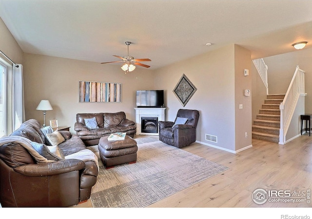 living area with light wood finished floors, visible vents, baseboards, stairway, and a fireplace