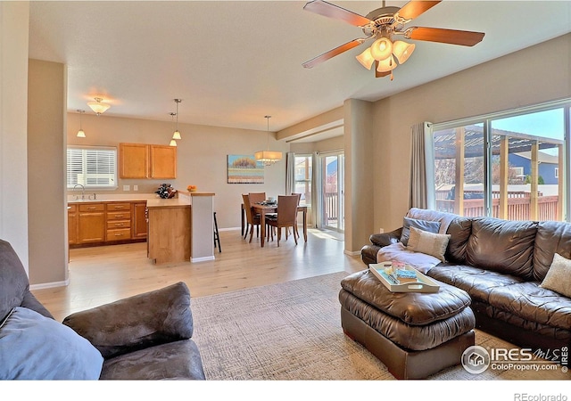 living room with a ceiling fan, baseboards, and light wood finished floors