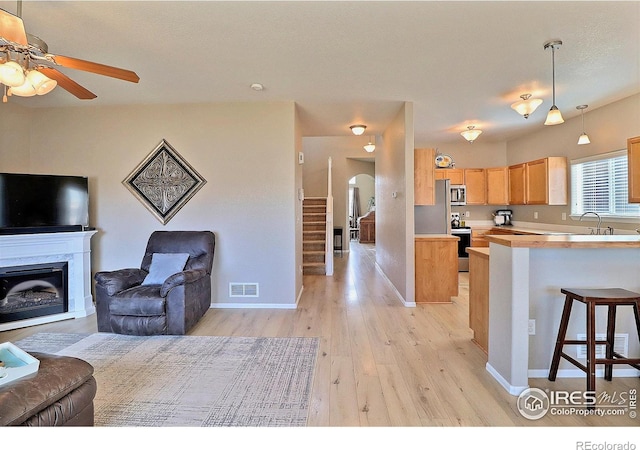 kitchen with visible vents, a kitchen bar, light brown cabinetry, open floor plan, and stainless steel appliances