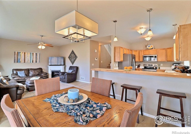 dining area with stairs, light wood-style flooring, a fireplace, and a ceiling fan