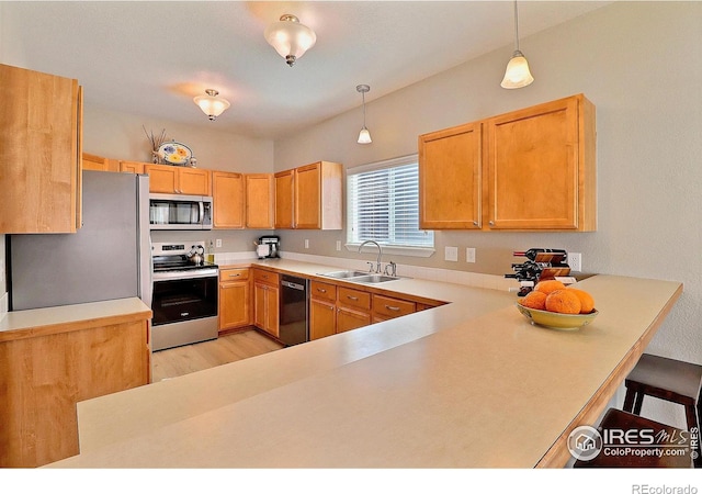 kitchen with a breakfast bar, a sink, hanging light fixtures, light countertops, and appliances with stainless steel finishes