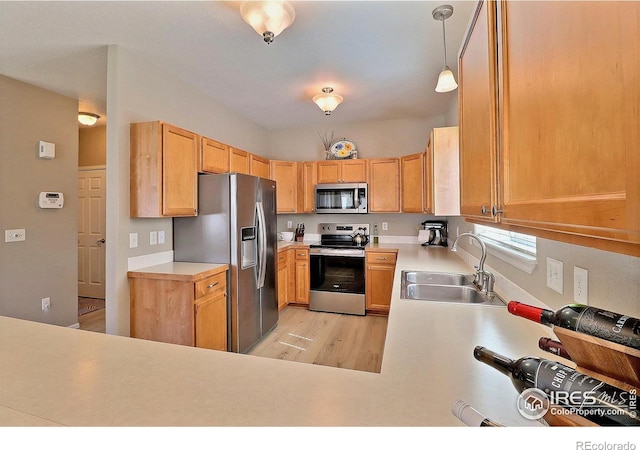 kitchen featuring a sink, light countertops, light wood-style floors, appliances with stainless steel finishes, and pendant lighting