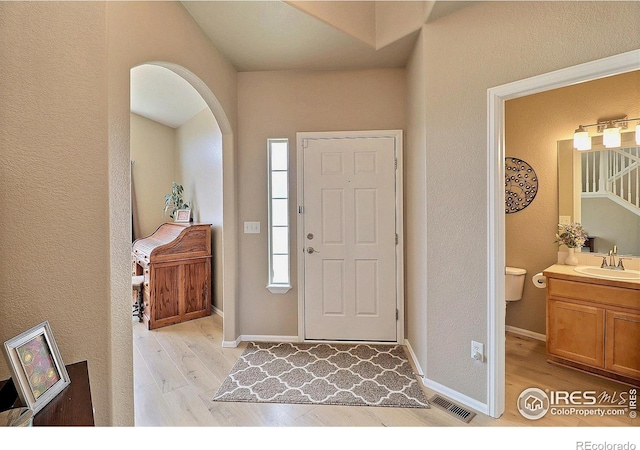 entrance foyer with arched walkways, visible vents, light wood-style flooring, and baseboards