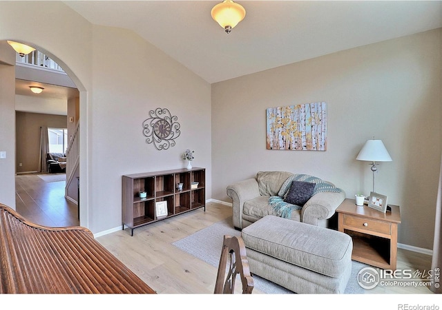 living room with arched walkways, baseboards, lofted ceiling, and wood finished floors