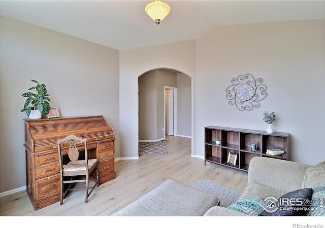 office featuring lofted ceiling, light wood-style floors, arched walkways, and baseboards