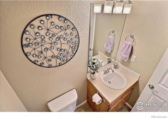 bathroom with toilet, vanity, and a textured wall