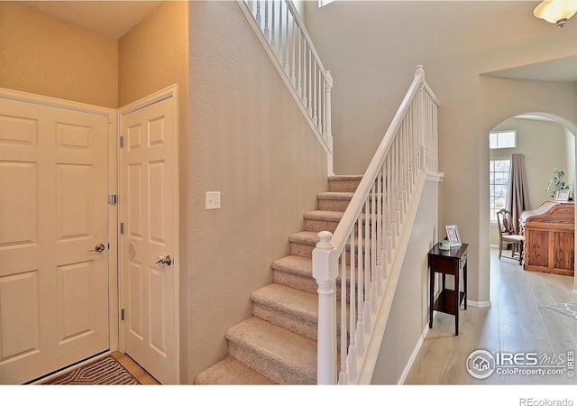 staircase with baseboards, arched walkways, and wood finished floors